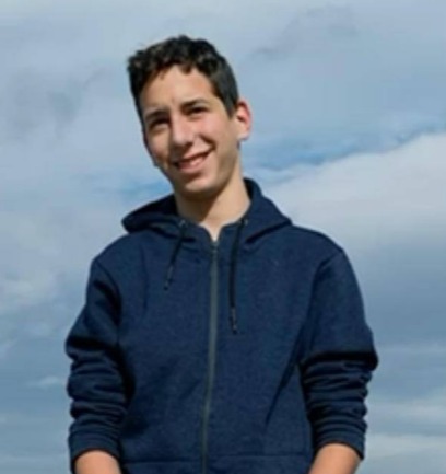 a young man in a blue hoodie stands with his hands folded