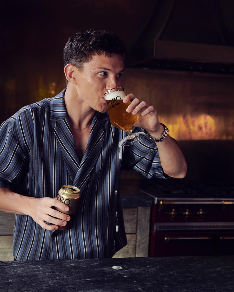 a man in a striped shirt is drinking a beer from a glass
