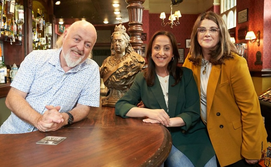 three people posing for a picture in front of a statue of queen victoria