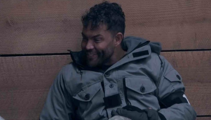 a man in a gray jacket is sitting on a wooden bench .