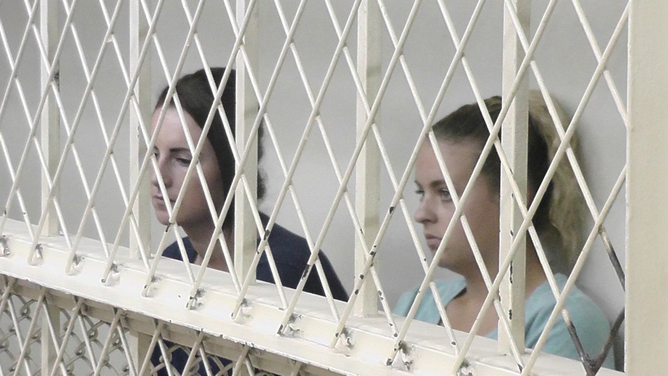 two women are behind a wire fence looking out