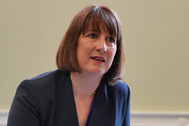a woman wearing a blue jacket and a necklace looks at the camera