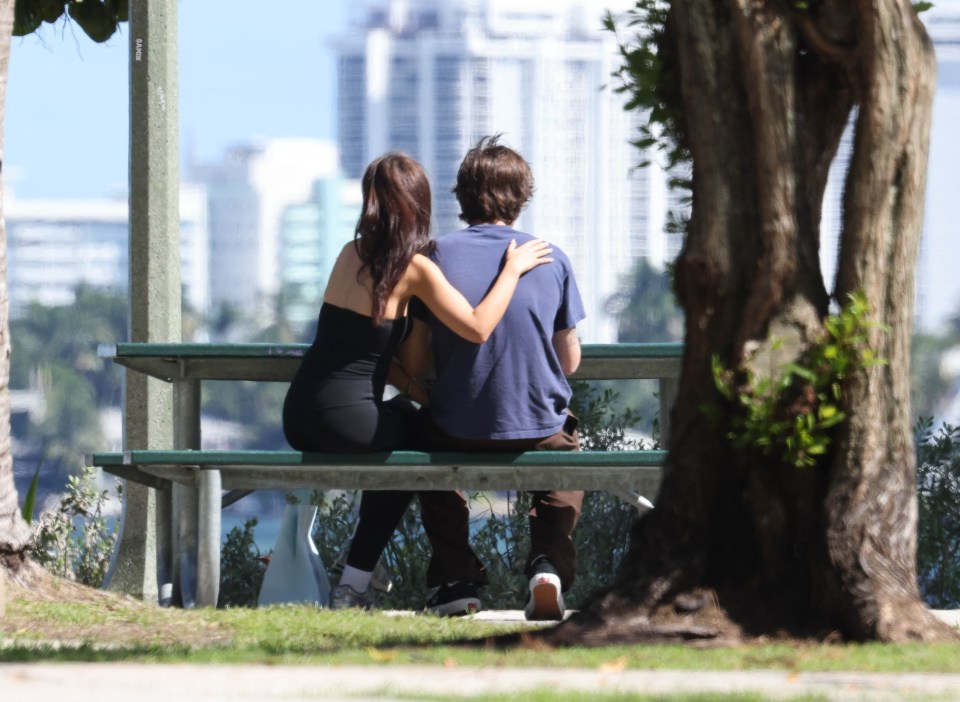 a man and a woman sit on a picnic table with a city in the background