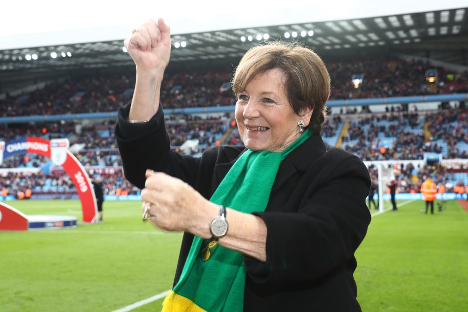 a woman wearing a green scarf and a watch stands on a soccer field