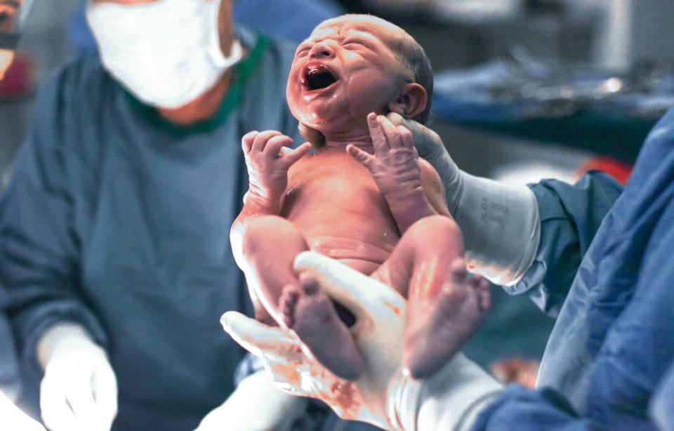 a newborn baby is being held by a surgeon in an operating room