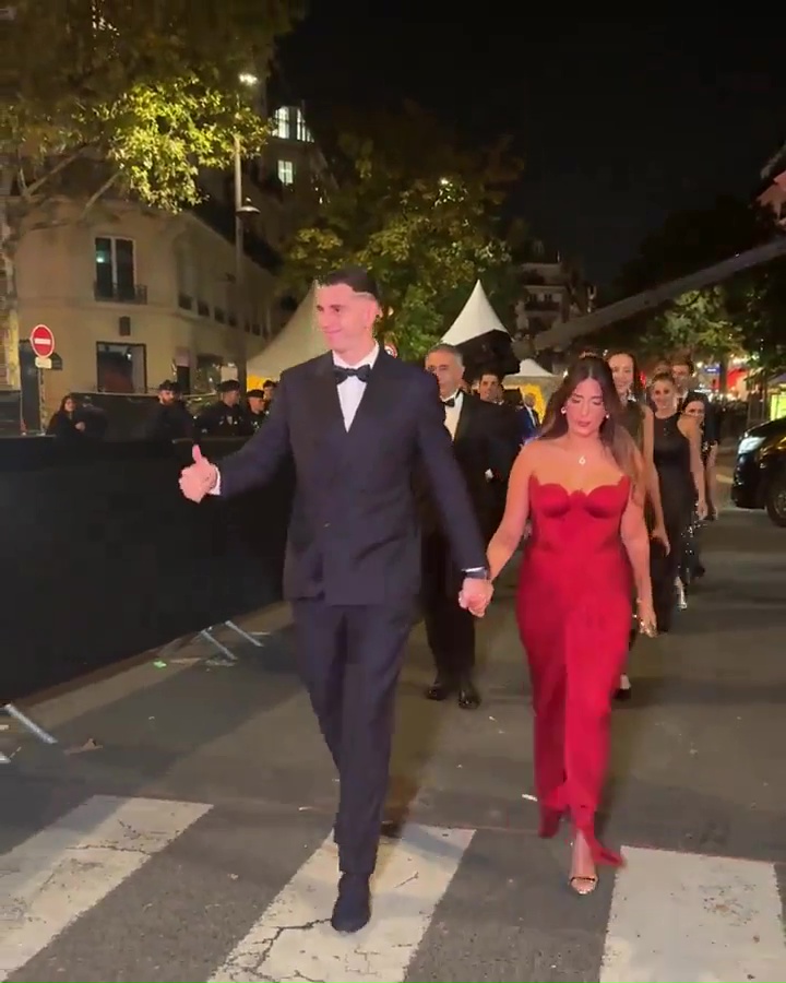 a man in a tuxedo is walking with a woman in a red dress