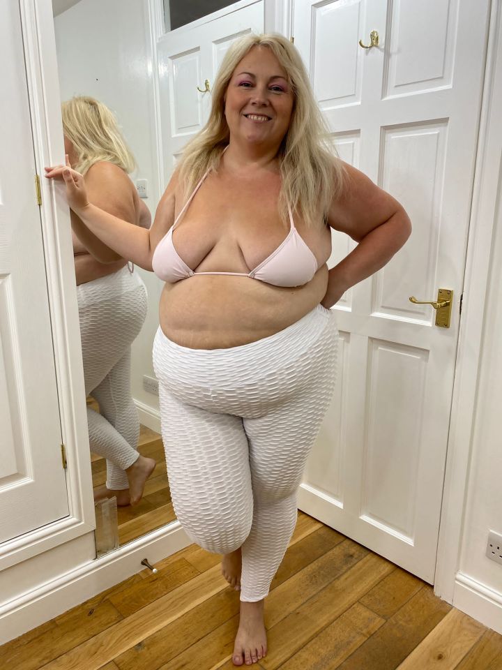 a woman in a bikini top and white pants stands in front of a mirror