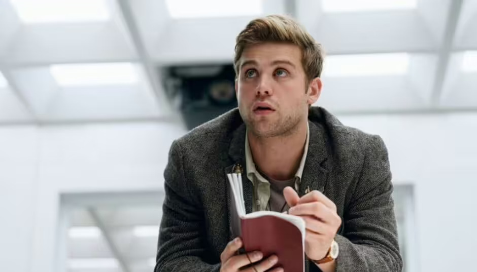 a man in a suit is holding a notebook and looking up .