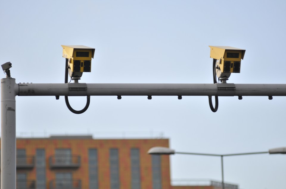 two yellow traffic cameras on a pole with a building in the background