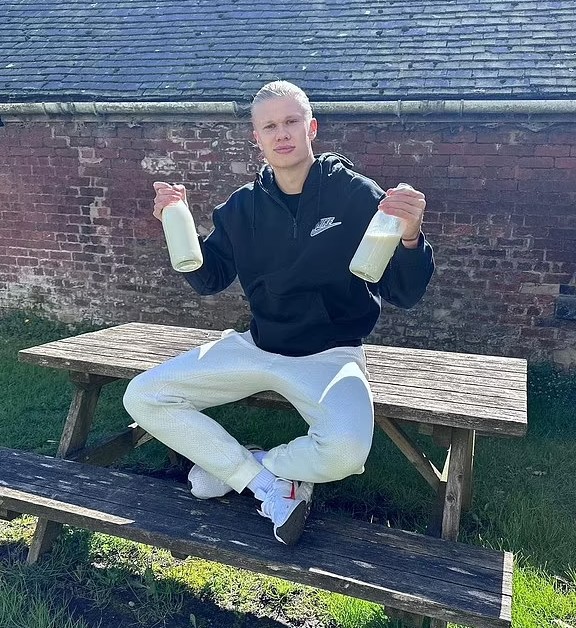 a man is sitting on a picnic table holding two bottles of milk .