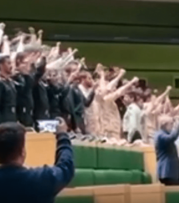 a man is taking a picture of a crowd of people raising their hands in the air .