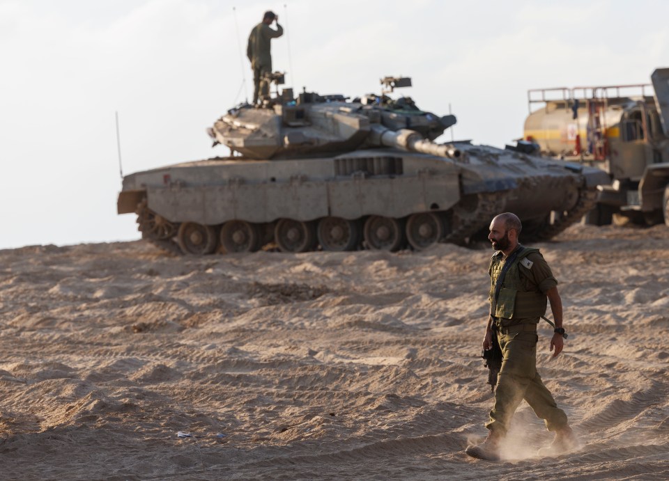 a soldier walking in the sand with a tank in the background