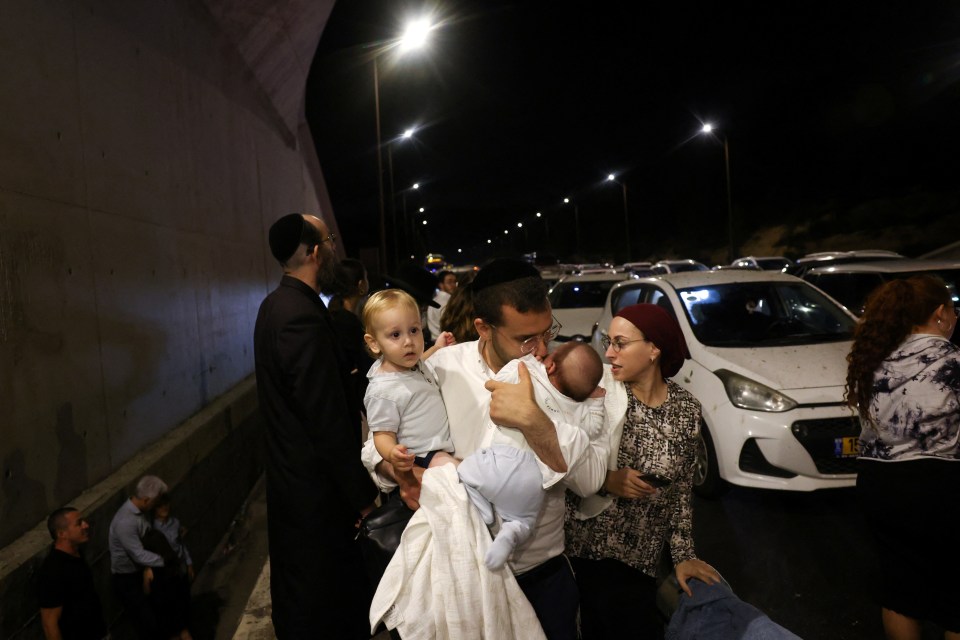 a man carrying a baby talks to a woman in front of a hyundai car