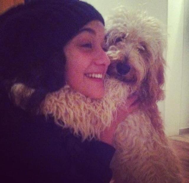 a woman in a black hat is hugging a small brown dog