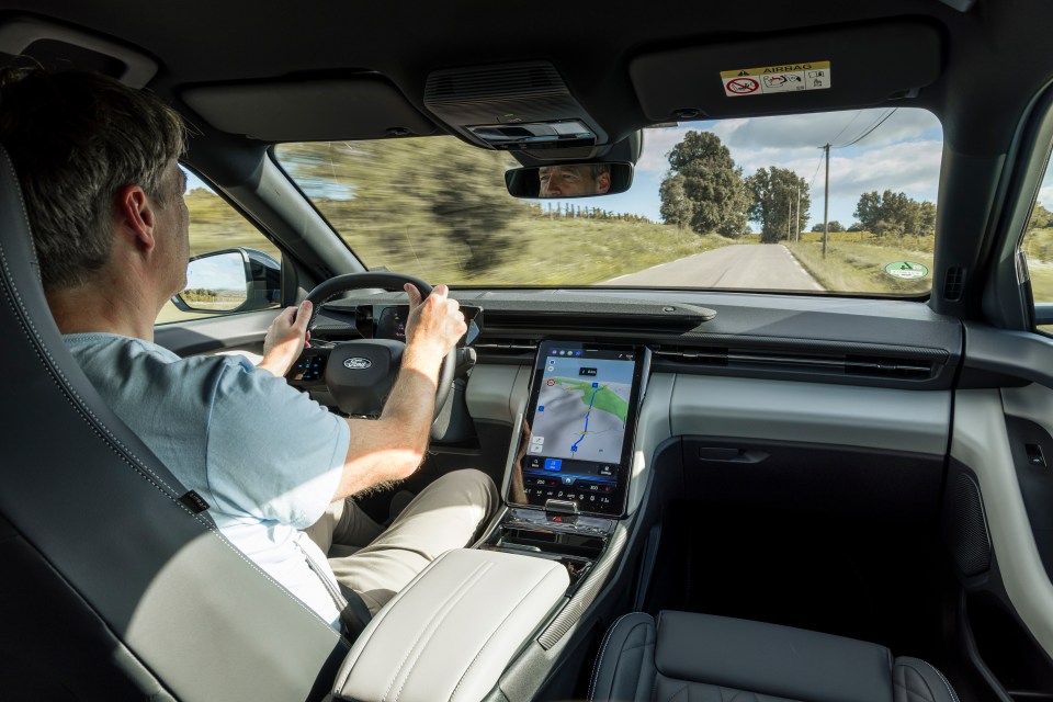 a man is driving a car with a phone on the dashboard