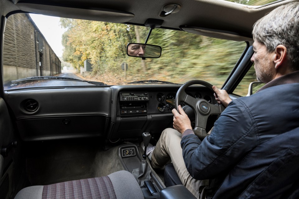 a man driving a car with a ford logo on the steering wheel