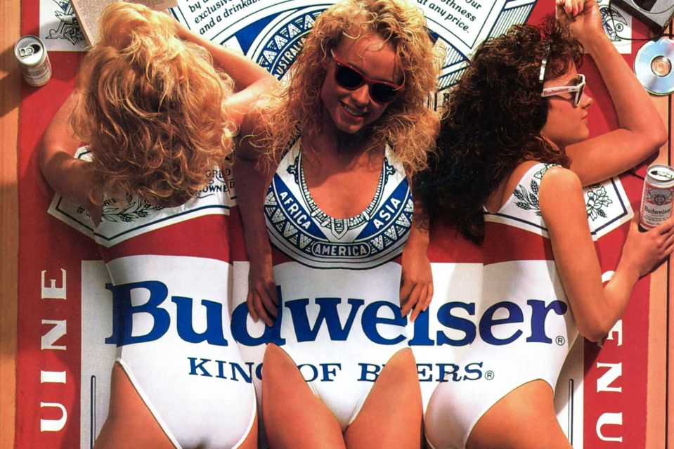 three women in swimsuits are laying on a budweiser towel