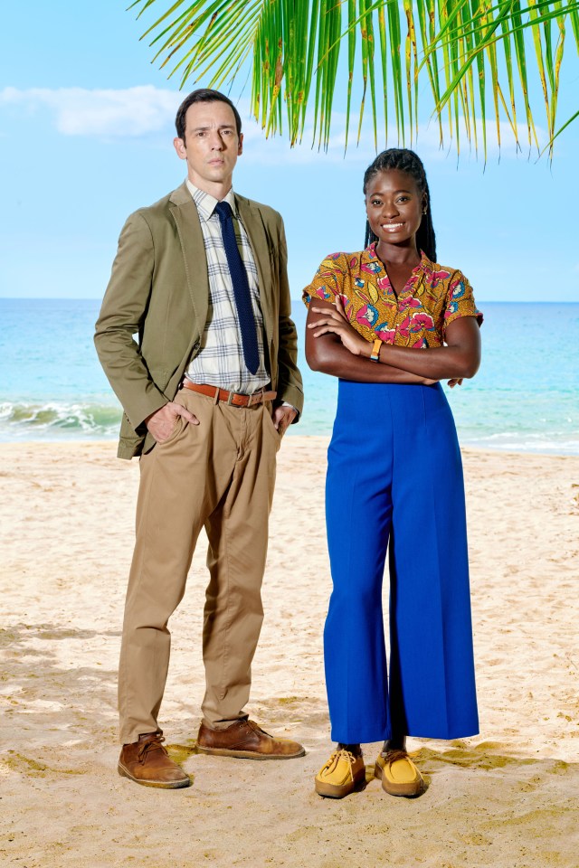 a man and a woman standing on a beach with their arms crossed