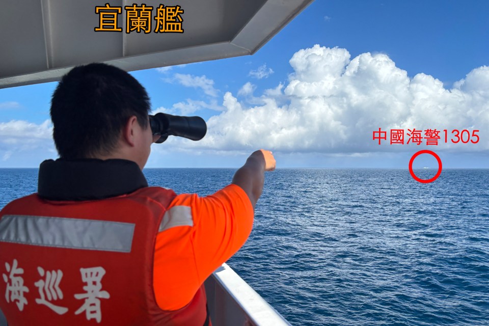 a man wearing a red vest with chinese writing on it looks out over the ocean
