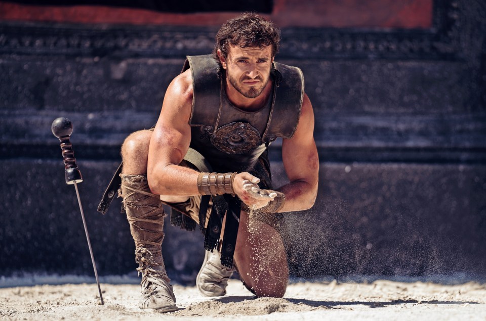 a man in a gladiator costume is kneeling in the sand