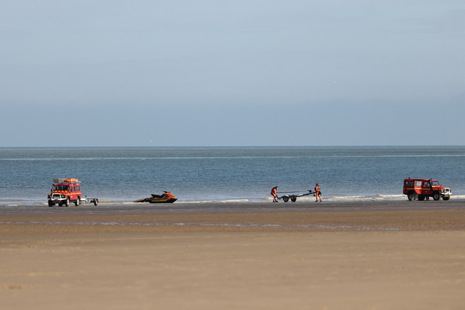 a group of people carrying a jet ski on a trailer on a beach