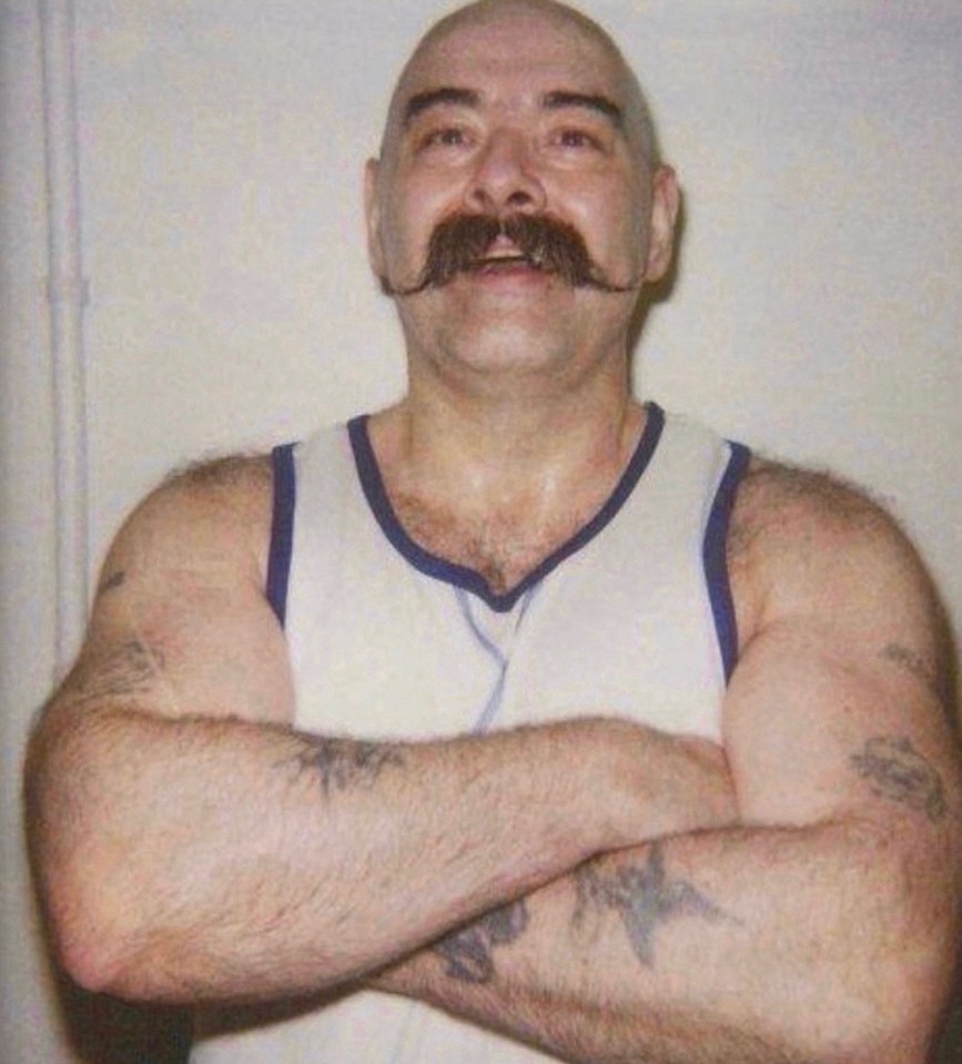 a bald man with a mustache is standing with his arms crossed