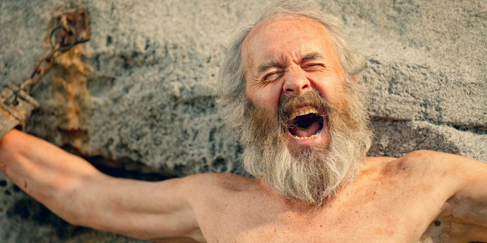a shirtless man with a beard is chained to a rock with his mouth open