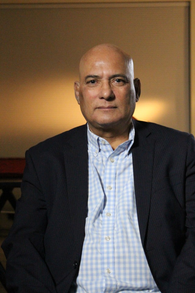 a bald man in a suit and plaid shirt looks at the camera