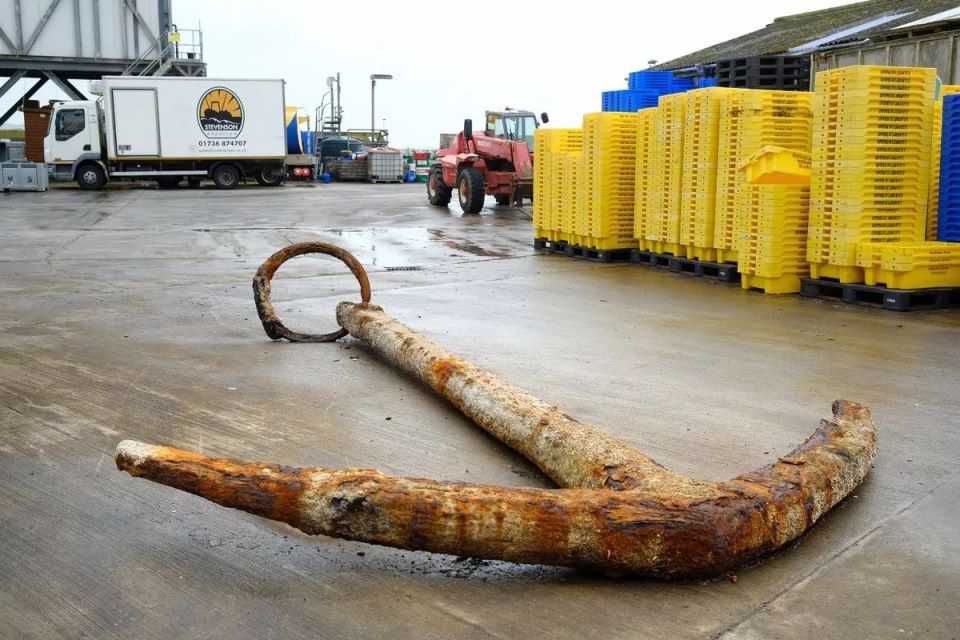 a rusty anchor sits in front of a stack of yellow crates