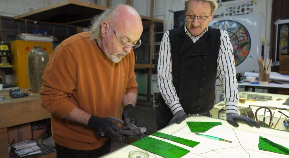 two men are working on a piece of green glass
