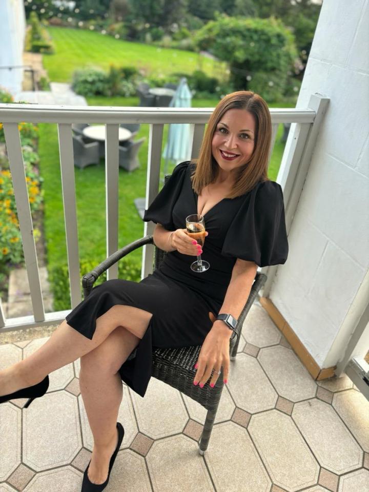 a woman in a black dress is sitting in a chair holding a glass of wine