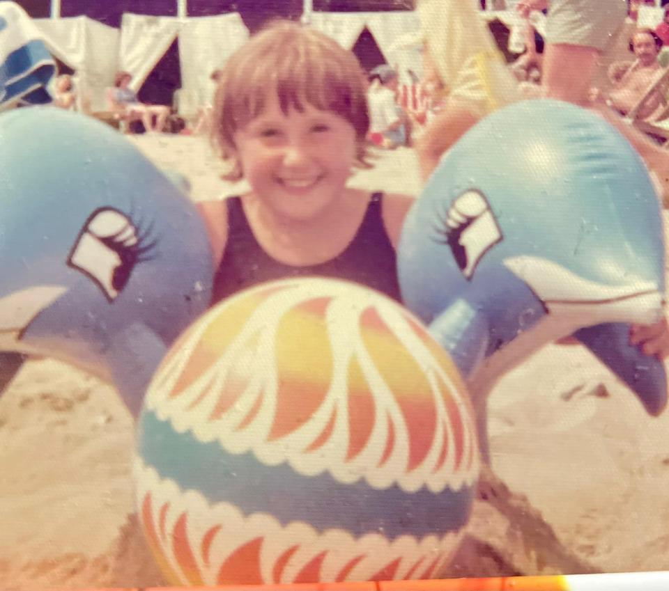 a girl is holding a beach ball in the shape of a dolphin