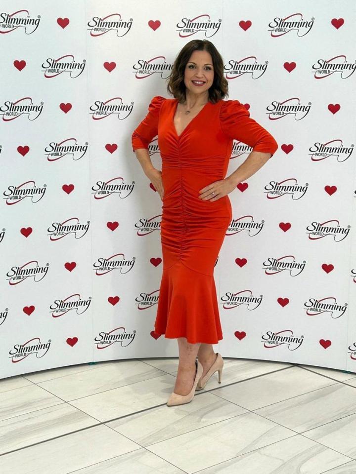 a woman in a red dress stands in front of a wall that says slimming