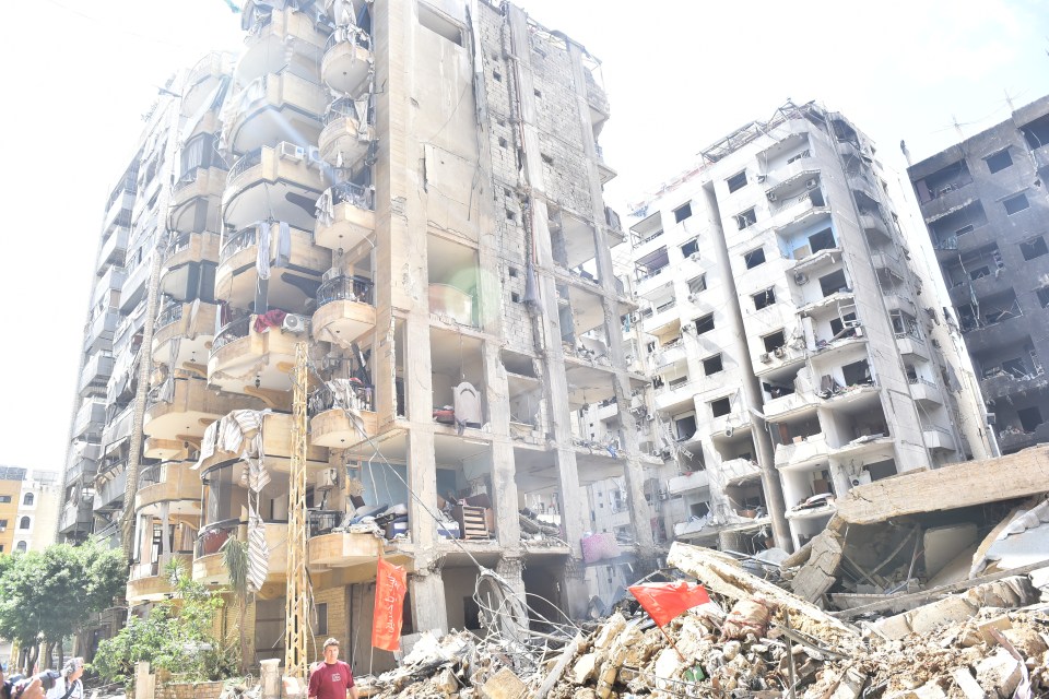 a man in a red shirt stands in front of a building that has been demolished