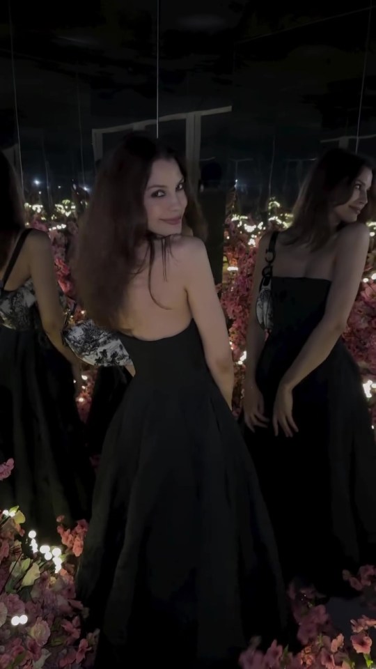 a woman in a black dress is standing in front of a mirror