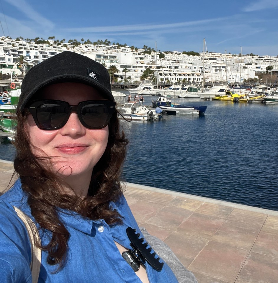 a woman wearing sunglasses and a black hat stands in front of a marina