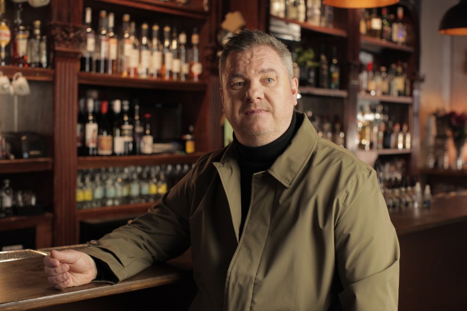 a man in a green coat leans on a bar counter