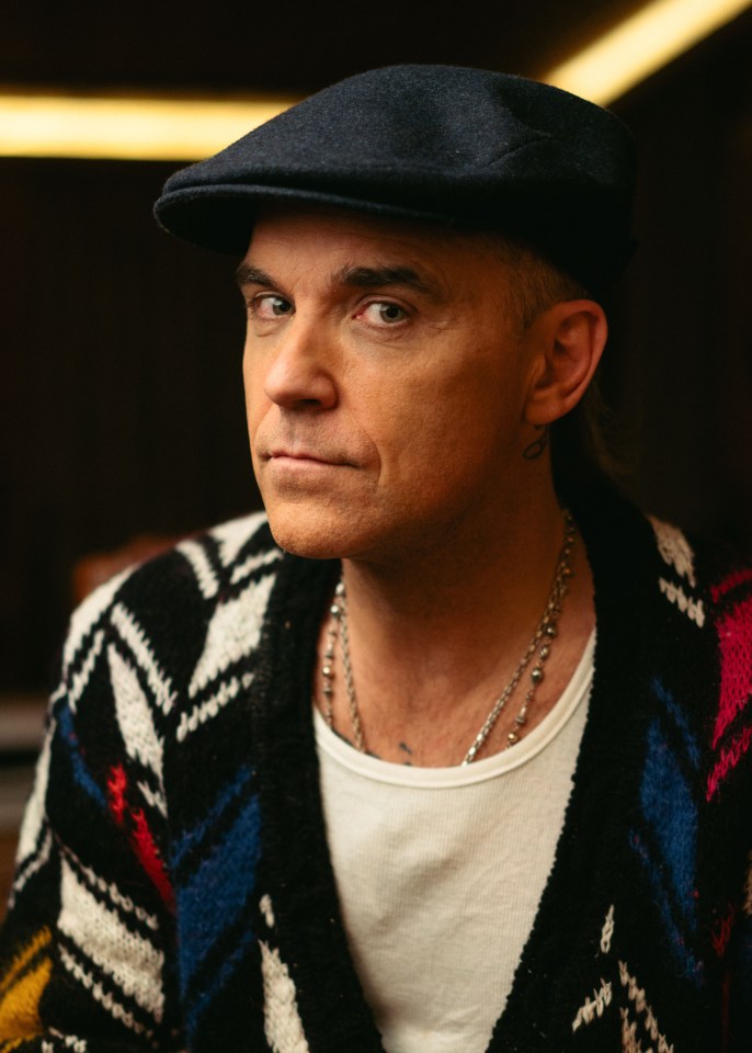 a man wearing a hat and a sweater looks at the camera