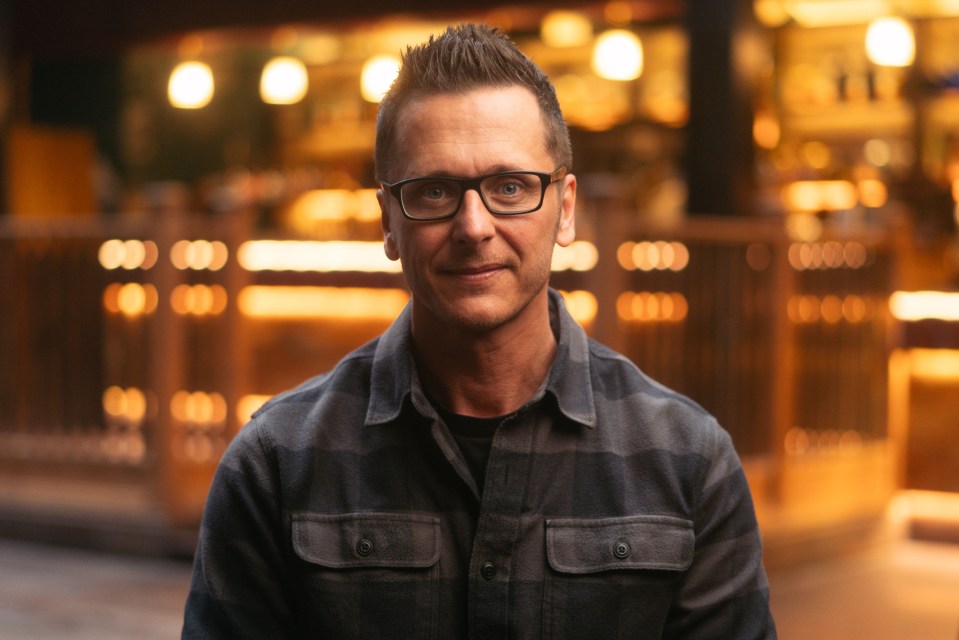 a man wearing glasses and a plaid shirt looks at the camera