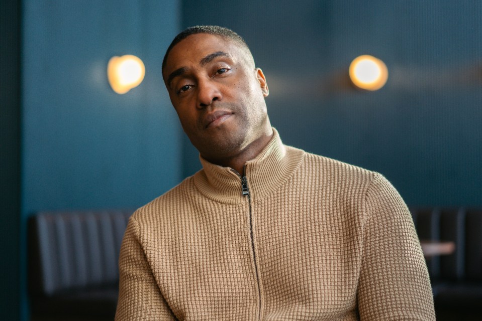 a man in a tan sweater looks at the camera