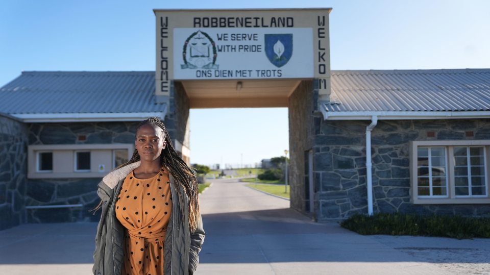 a woman stands in front of a sign that says robbeneiland