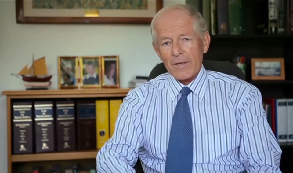 a man in a striped shirt and tie sits in front of a bookshelf with binders on it
