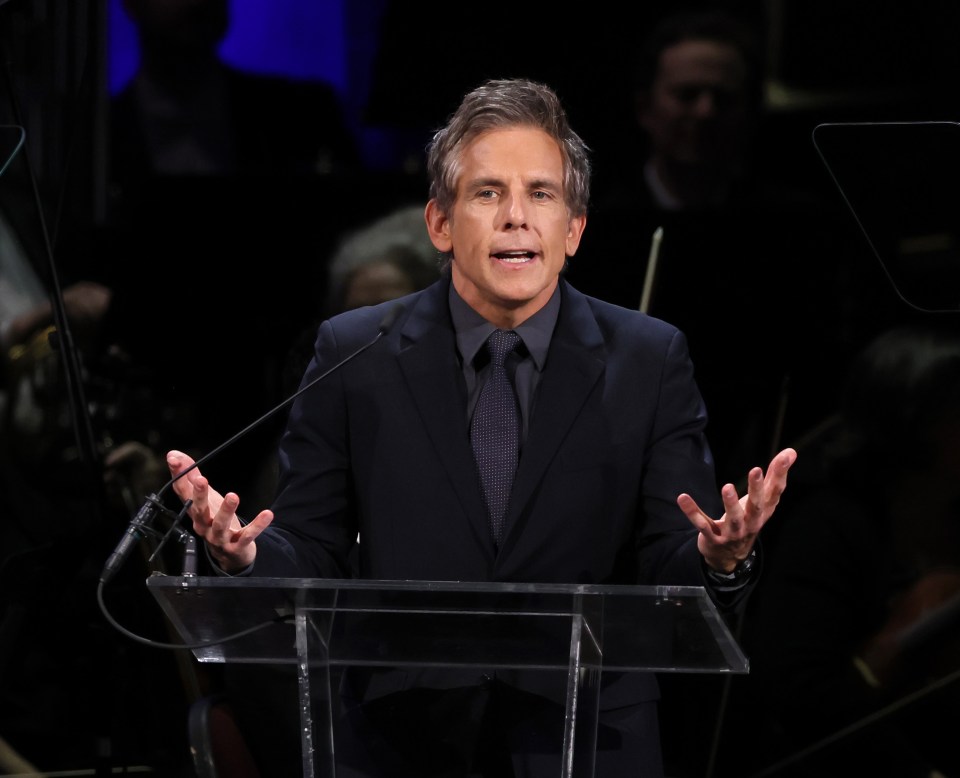 a man in a suit and tie stands at a podium speaking into a microphone