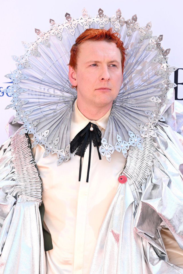 a man with red hair is wearing a white shirt and a silver cape