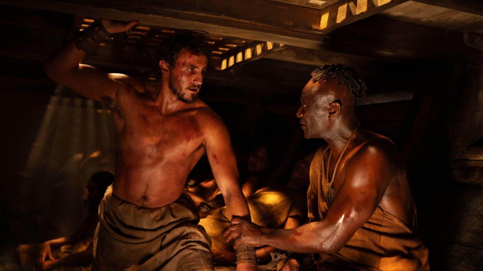 a man without a shirt is talking to another man in a dark room