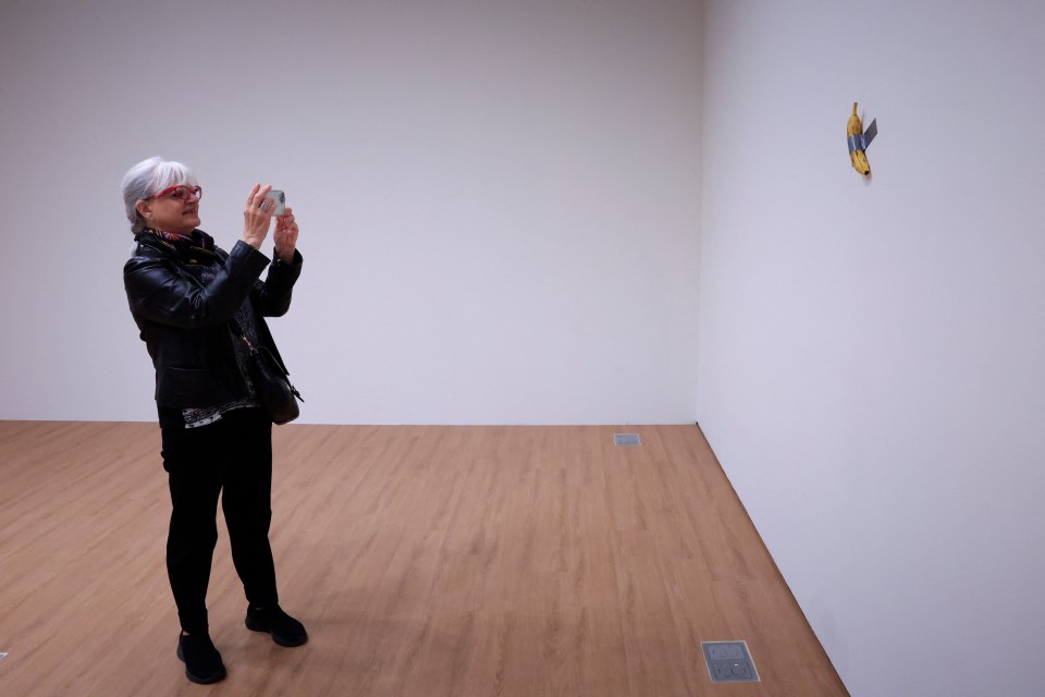 a woman taking a picture of a banana on a wall