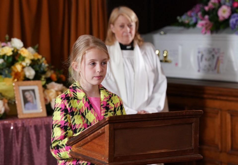 a little girl stands at a podium in front of a coffin