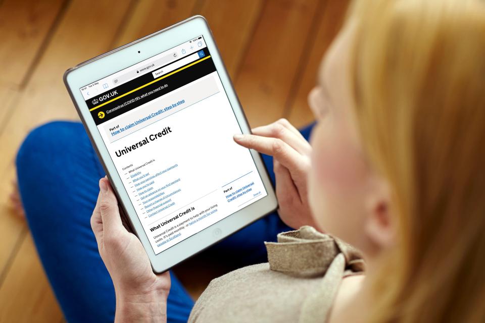 a woman is looking at a tablet that says universal credit on the screen