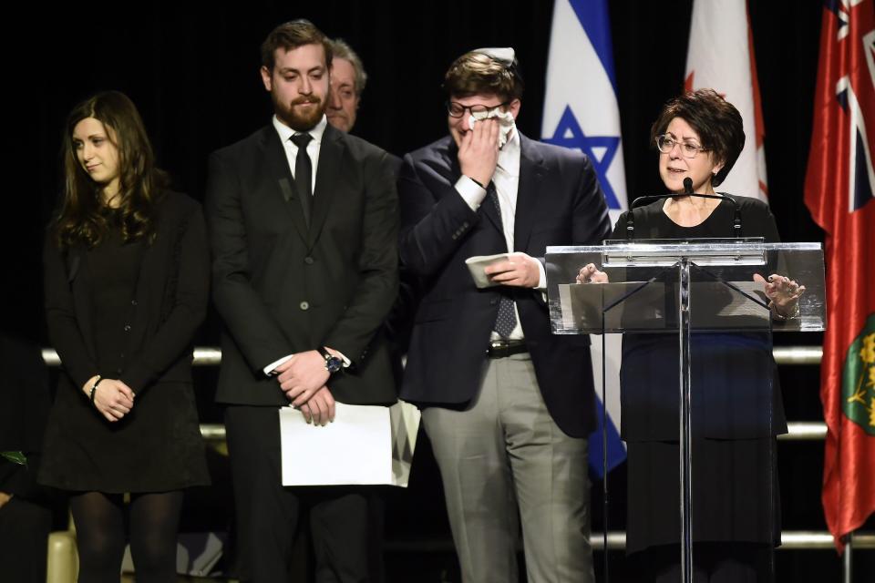 a woman stands at a podium while a man wipes his face