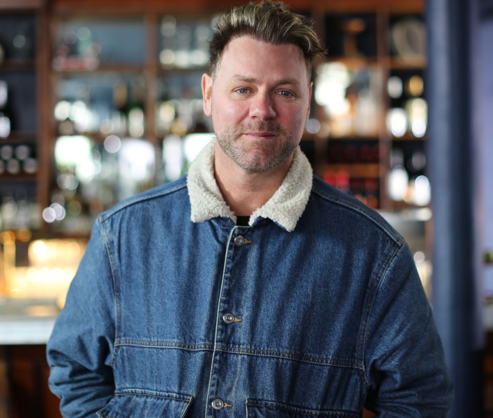 a man in a denim jacket stands in front of a bar